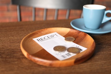 Photo of Tips, receipt and cup of drink on wooden table in cafe, closeup