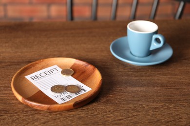 Photo of Tips, receipt and cup of drink on wooden table in cafe, closeup