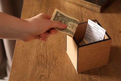 Photo of Woman putting tips into box at wooden table indoors, closeup