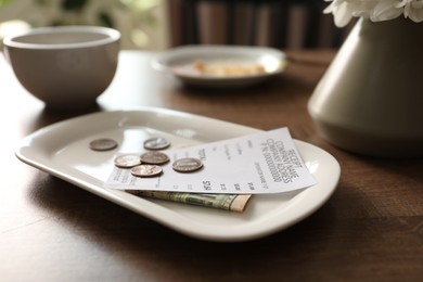 Photo of Tips, receipt, dirty plate and cup on wooden table in cafe, closeup