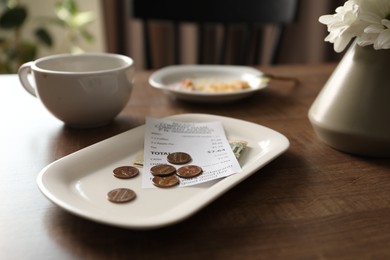 Photo of Tips, receipt, dirty plate and cup on wooden table in cafe, closeup