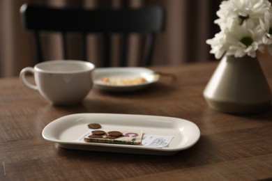 Photo of Tips, receipt, chrysanthemum flowers, dirty plate and cup on wooden table in cafe, closeup