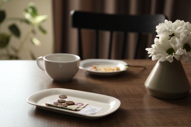 Photo of Tips, receipt, chrysanthemum flowers, dirty plate and cup on wooden table in cafe, closeup
