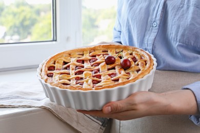 Photo of Woman holding tasty cherry pie indoors, closeup