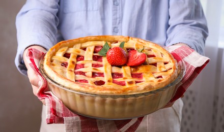 Photo of Woman holding tasty strawberry pie indoors, closeup