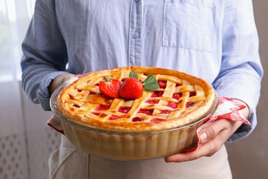 Photo of Woman holding tasty strawberry pie indoors, closeup