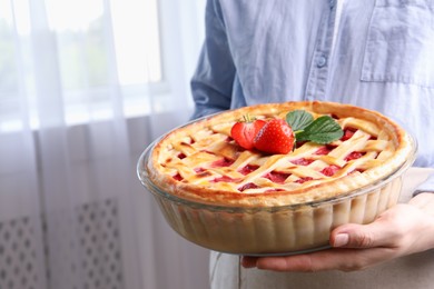 Photo of Woman holding tasty strawberry pie indoors, closeup