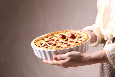Photo of Woman holding tasty cherry pie on light brown background, closeup