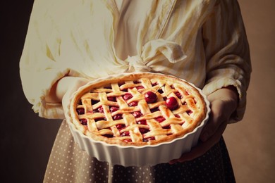 Photo of Woman holding tasty cherry pie on light brown background, closeup