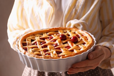 Photo of Woman holding tasty cherry pie on light brown background, closeup