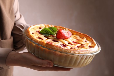 Photo of Woman holding tasty strawberry pie on light brown background, closeup