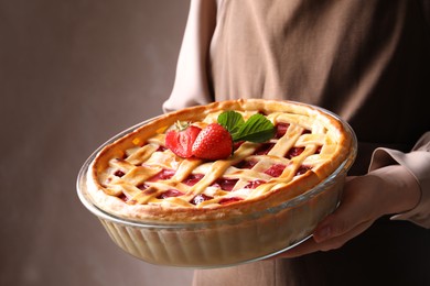 Photo of Woman holding tasty strawberry pie on light brown background, closeup