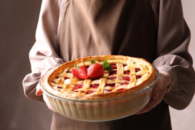 Photo of Woman holding tasty strawberry pie on light brown background, closeup