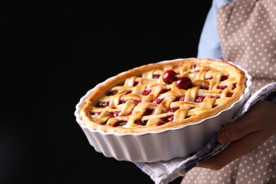 Photo of Woman holding tasty cherry pie on black background, closeup
