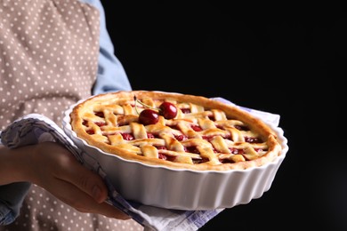 Photo of Woman holding tasty cherry pie on black background, closeup