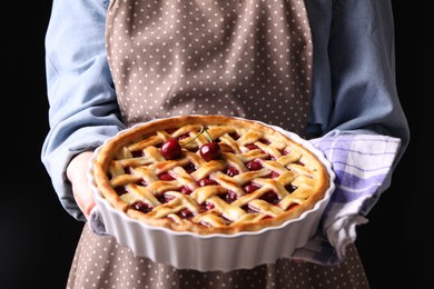 Photo of Woman holding tasty cherry pie on black background, closeup
