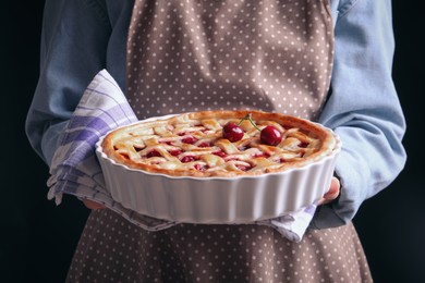 Photo of Woman holding tasty cherry pie on black background, closeup