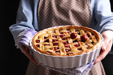 Photo of Woman holding tasty cherry pie on black background, closeup