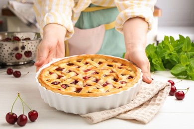 Photo of Woman with tasty cherry pie at white wooden table, closeup