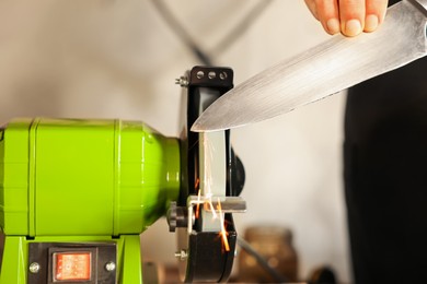 Photo of Man sharpening knife with bench grinder indoors, closeup