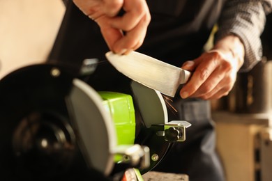Photo of Man sharpening knife with bench grinder indoors, closeup
