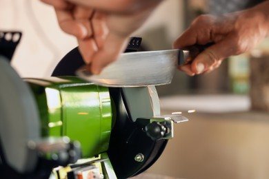 Photo of Man sharpening knife with bench grinder indoors, closeup