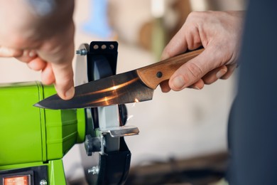 Photo of Man sharpening knife with bench grinder indoors, closeup