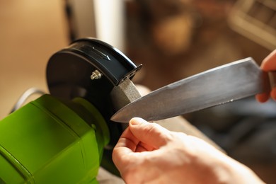 Photo of Man sharpening knife with bench grinder indoors, above view