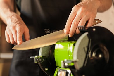 Photo of Man sharpening knife with bench grinder indoors, closeup