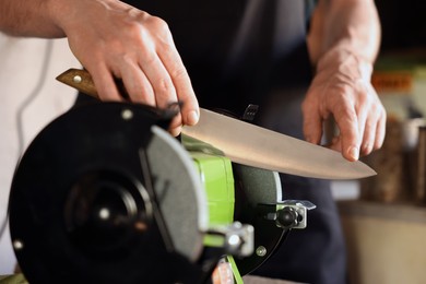 Photo of Man sharpening knife with bench grinder indoors, closeup
