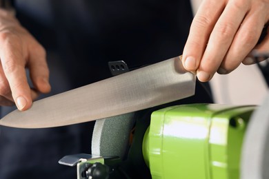 Photo of Man sharpening knife with bench grinder indoors, closeup