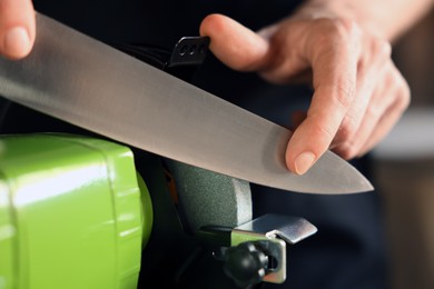 Photo of Man sharpening knife with bench grinder indoors, closeup