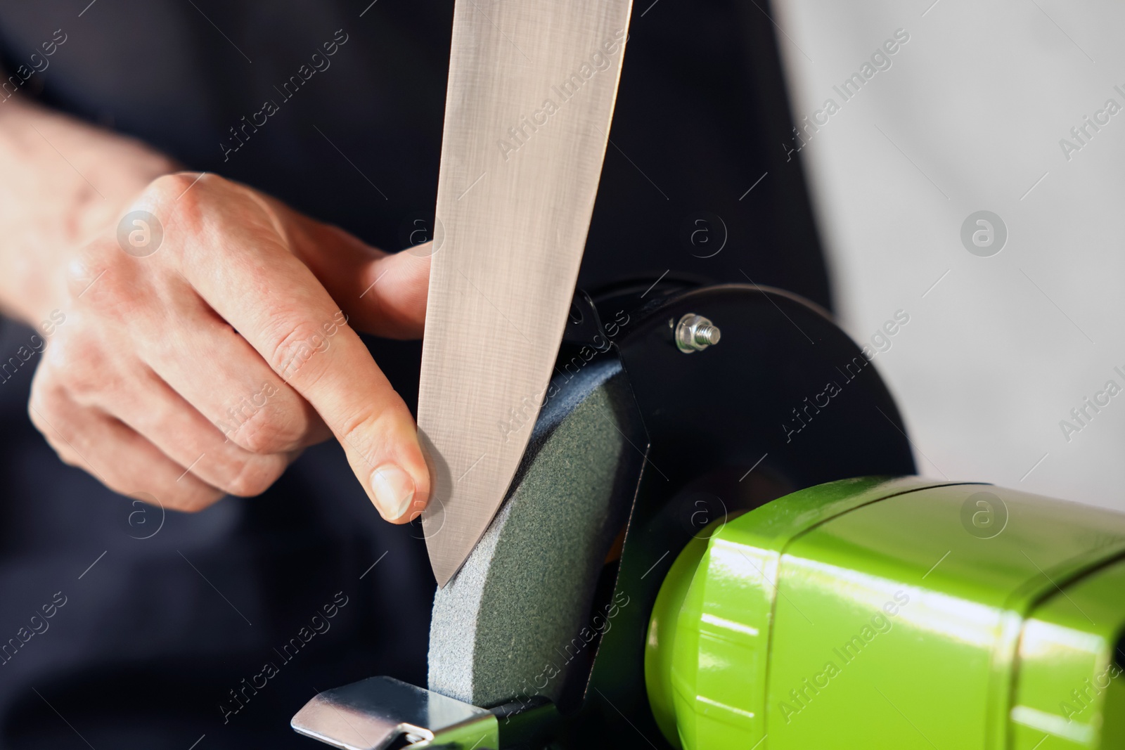 Man sharpening knife with bench grinder indoors, closeup Photo of Man sharpening knife with bench grinder indoors, closeup