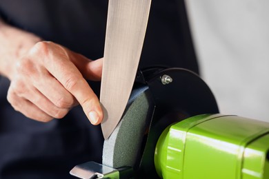 Photo of Man sharpening knife with bench grinder indoors, closeup