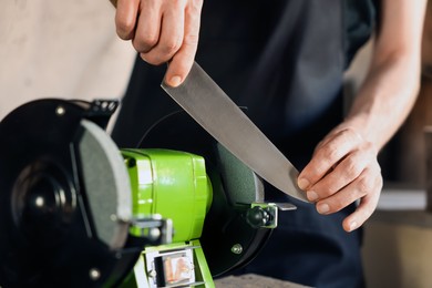 Photo of Man sharpening knife with bench grinder indoors, closeup