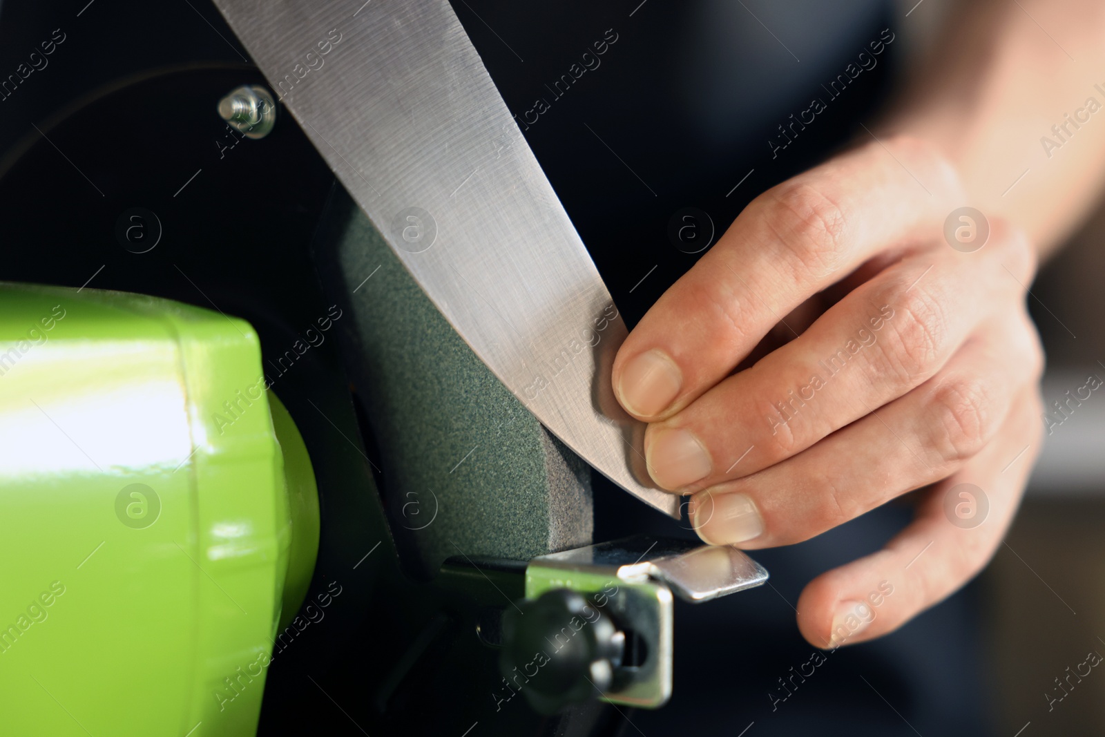 Man sharpening knife with bench grinder indoors, closeup Photo of Man sharpening knife with bench grinder indoors, closeup