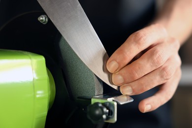 Photo of Man sharpening knife with bench grinder indoors, closeup