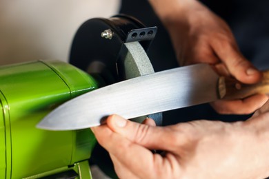 Photo of Man sharpening knife with bench grinder indoors, closeup