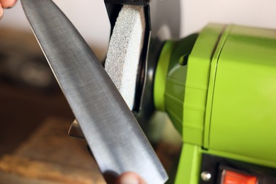 Photo of Man sharpening knife with bench grinder indoors, closeup