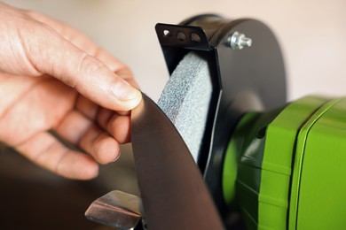 Photo of Man sharpening knife with bench grinder indoors, closeup