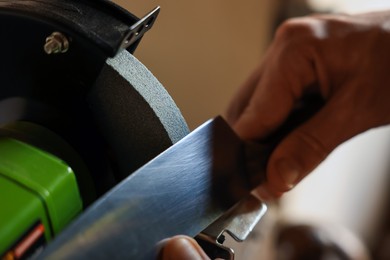Photo of Man sharpening knife with bench grinder indoors, closeup