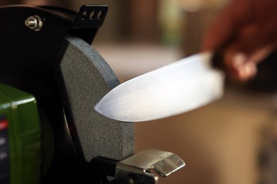 Photo of Man sharpening knife with bench grinder indoors, closeup