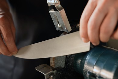 Photo of Man sharpening knife with bench grinder indoors, closeup