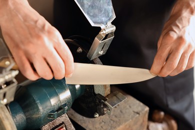 Photo of Man sharpening knife with bench grinder indoors, closeup