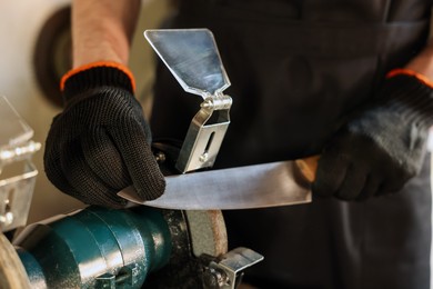 Photo of Man sharpening knife with bench grinder indoors, closeup