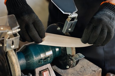 Photo of Man sharpening knife with bench grinder indoors, closeup