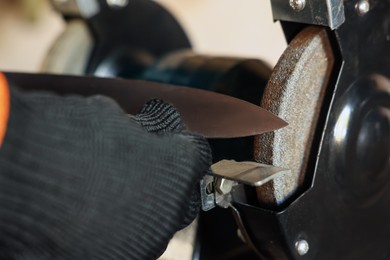 Photo of Man sharpening knife with bench grinder indoors, closeup