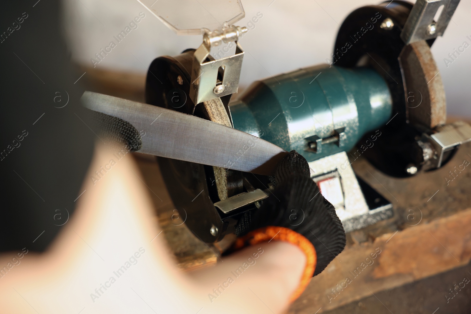 Man sharpening knife with bench grinder indoors, closeup Photo of Man sharpening knife with bench grinder indoors, closeup