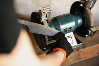Photo of Man sharpening knife with bench grinder indoors, closeup