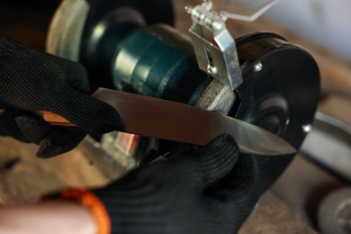 Photo of Man sharpening knife with bench grinder indoors, closeup